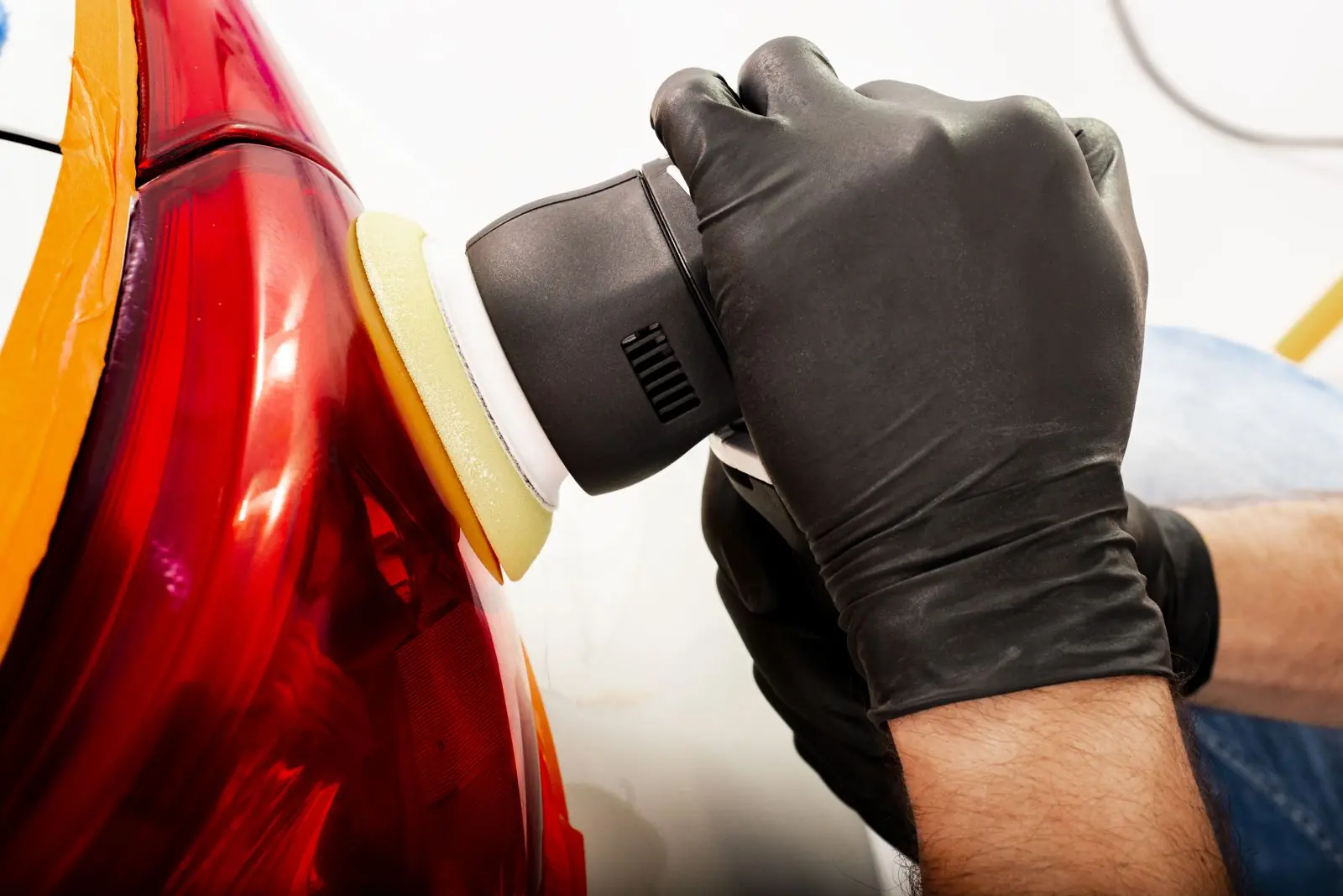 Detailer polishing a car bonnet beside a laptop showing a before-and-after gallery on a website