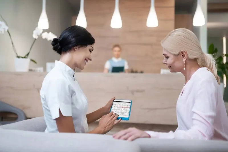 Clinic receptionist viewing an online appointment booking calendar on a tablet