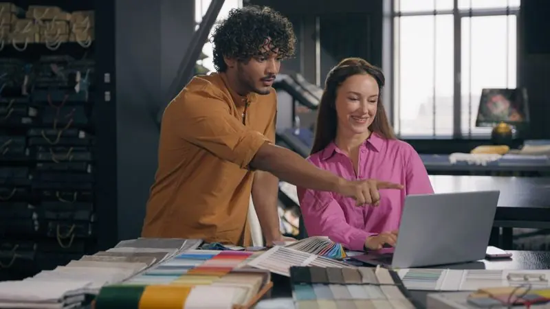 Designer at two monitors comparing a WordPress site build with a Webflow design canvas